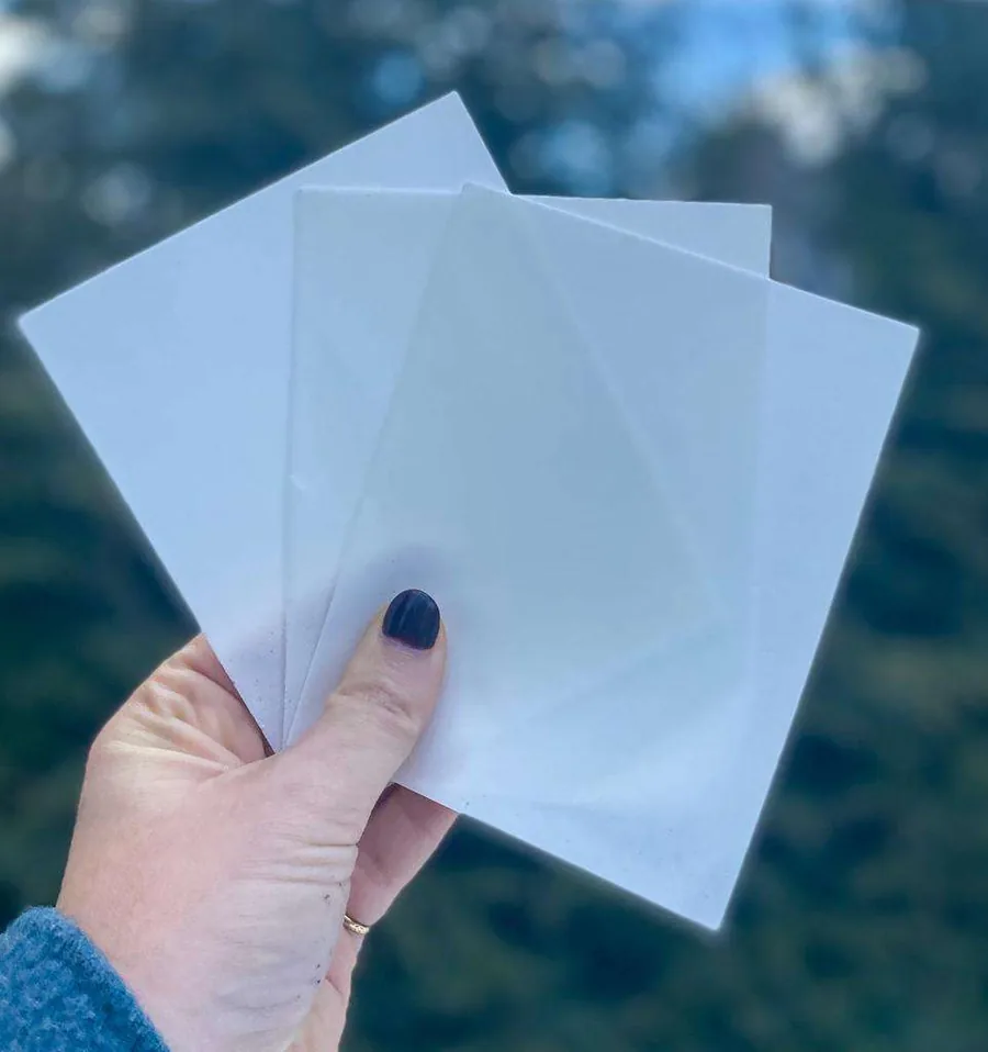 A hand holding three thin Spot detergent sheets